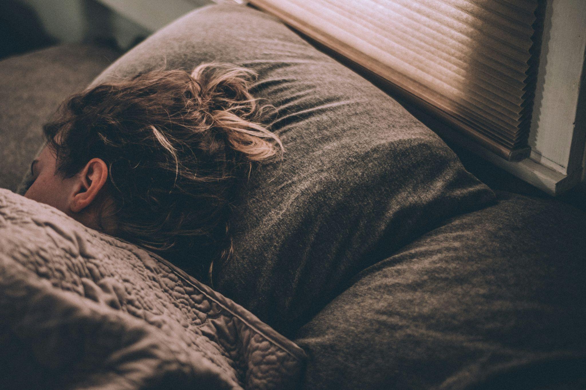 Person sleeping on their side in a dark, quiet bedroom, representing the importance of quality sleep for hormone balance and weight loss